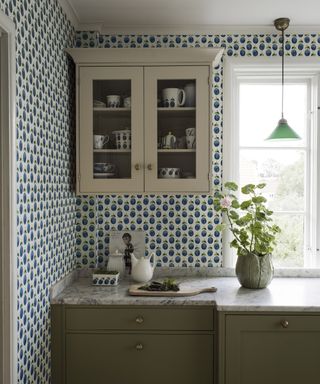 Blue and white patterned wall decor for kitchen with cream painted cabinet beside a window.