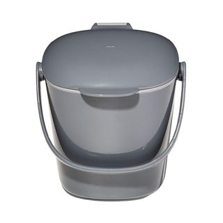 A dark gray compost bin with a curved gray handle in front of it and a large lid