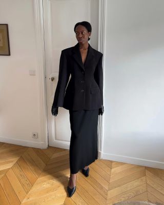 Sylvie is wearing an oversized black blazer, black maxi skirt, black leather gloves, and black heels.