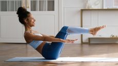 woman sitting on an exercise mat sideways to the camera balancing on her sit bones in a pilates one hundred move