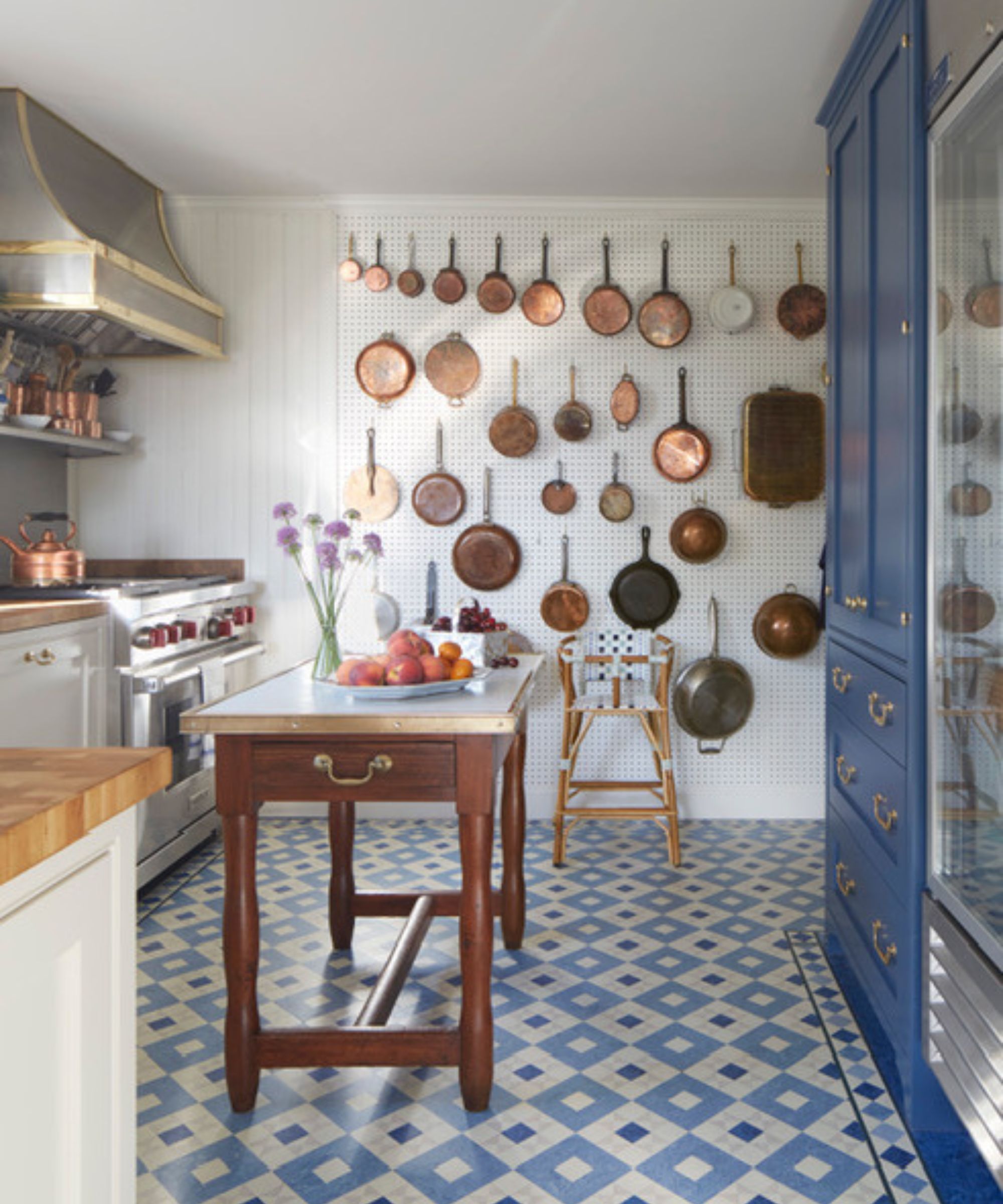 A traditional small kitchen with white cabinets, wooden countertops, stainless steel appliances, and a large pegboard for extra storage
