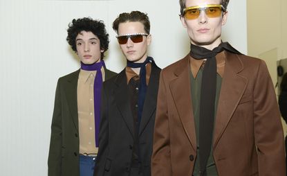 Three models stood with prada jackets on and scarf tied around neck