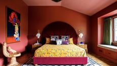 red color drenched bedroom with yellow sheets and throw pillows, a large artwork and hand-shaped seat, and velvet red headboard