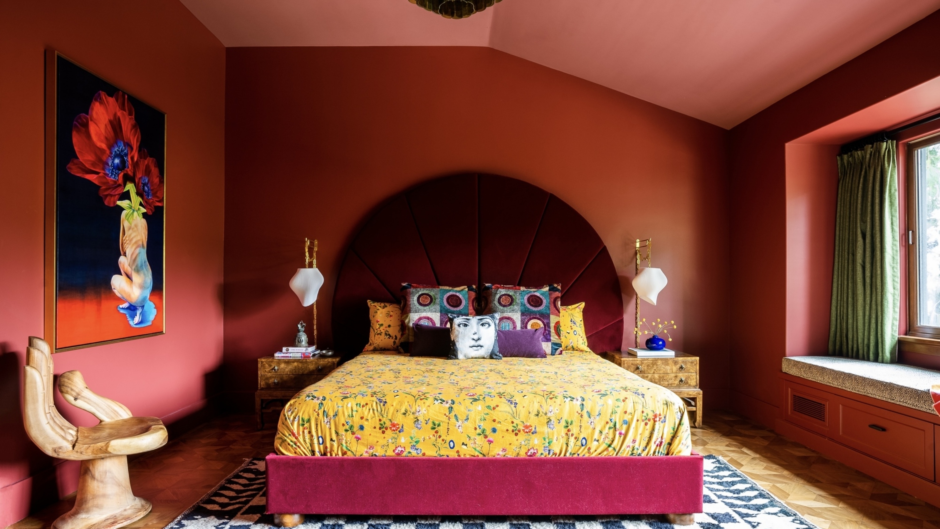 red color drenched bedroom with yellow sheets and throw pillows, a large artwork and hand-shaped seat, and velvet red headboard