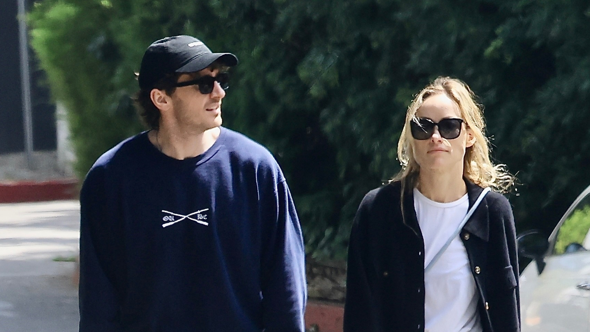 Olivia Wilde wearing a navy shirt, white t-shirt, blue jeans, and yellow sneakers