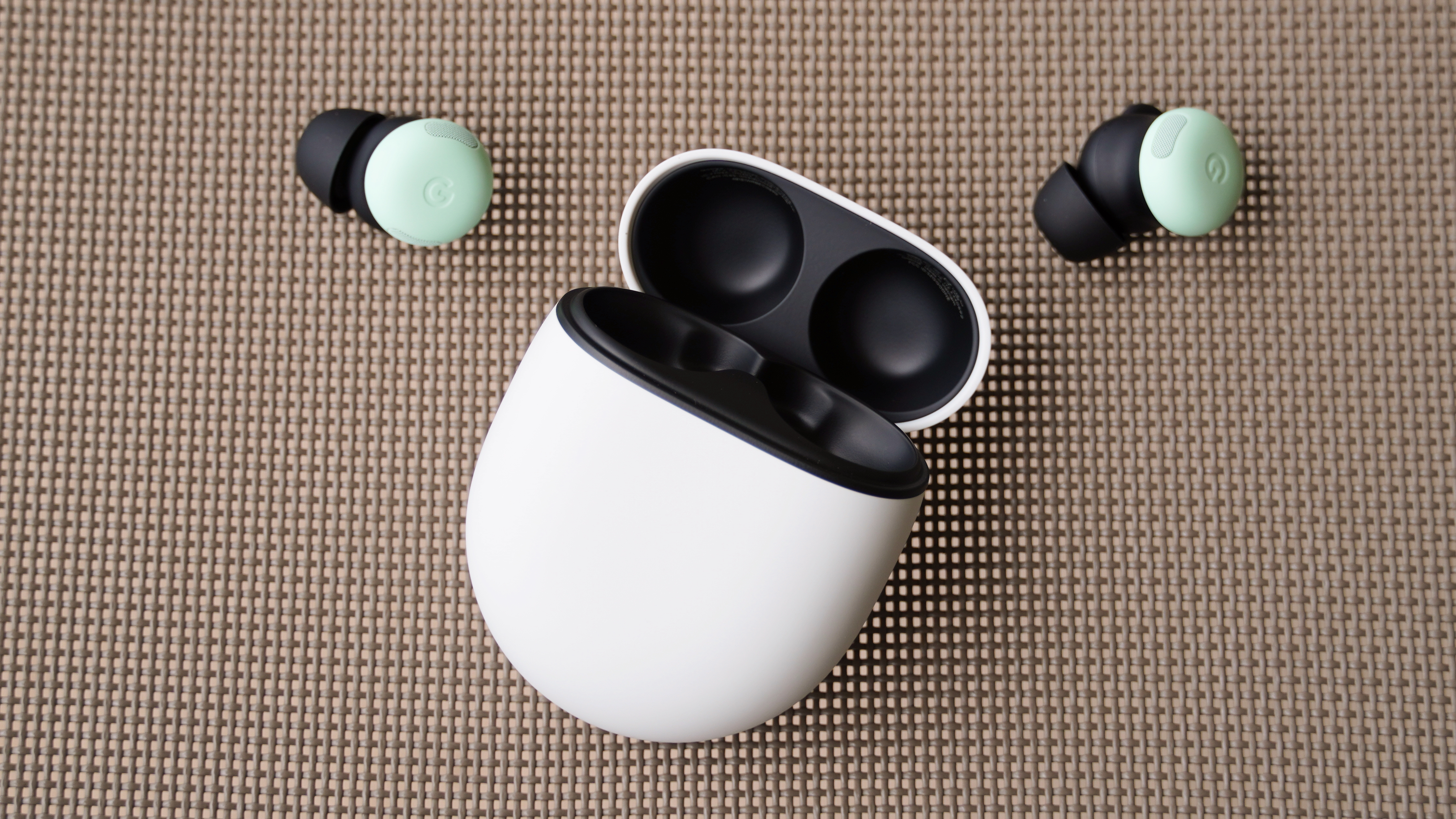The Google Pixel Buds Pro 2 in the Mint colorway beside their charging case.