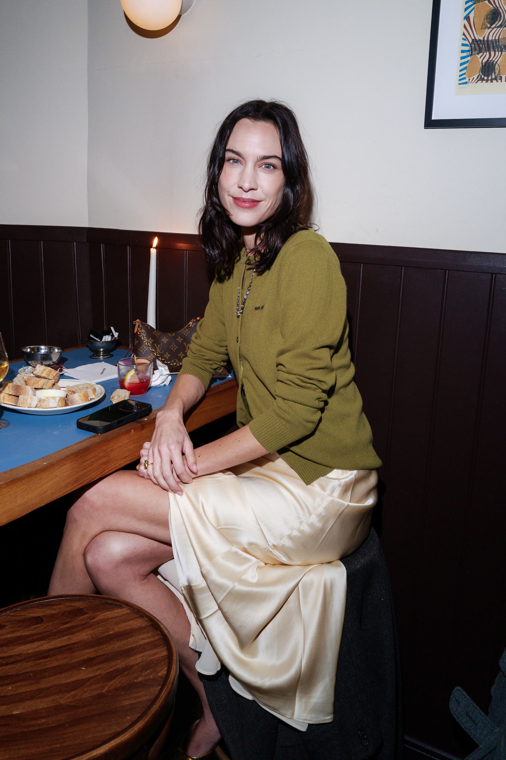 An image of Alexa Chung wearing a Reformation slip dress, grey coat, olive cardigan and gold heels.