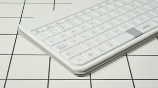 a closeup shot of the left side of a white, lightweight tablet keyboard made by mokibo rests upon a white tiled table with a blue background