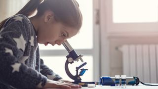 Here's a look at the best microscopes for kids. Shown here, a girl looking through a microscope.