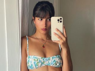 A woman taking a mirror selfie wearing a blue, white, and green floral ruched bikini top