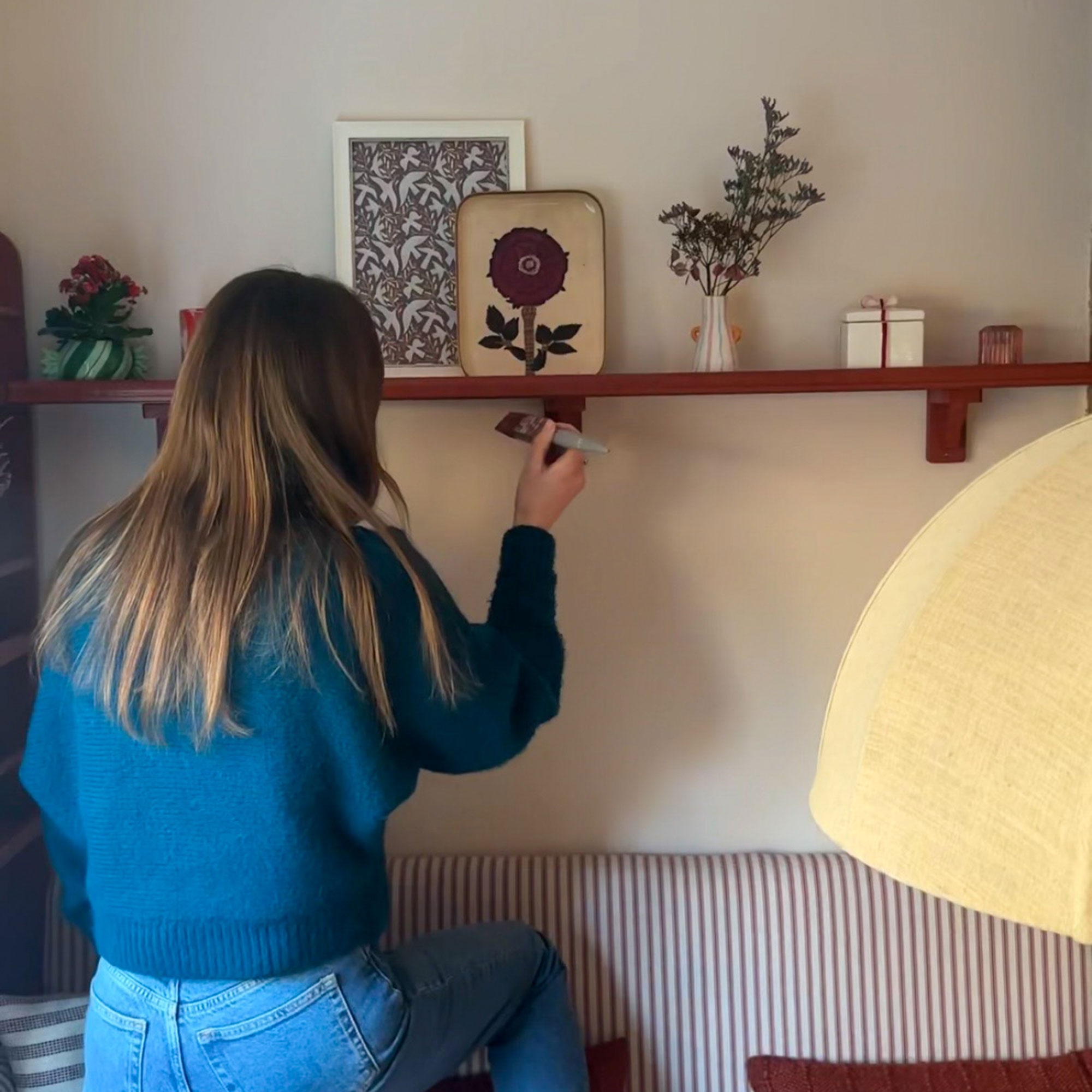 Woman painting red shelf above striped banquette