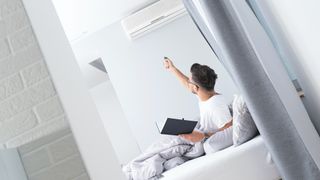 Man in bed controlling central air conditioner with remote