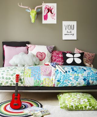 Girls' bedroom ideas with multi-coloured bedding and artwork against a dark green-gray painted wall.