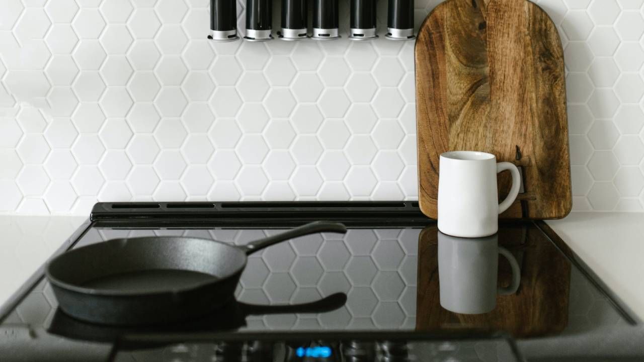 A lifestyle image of an induction hob with a saucepan, mug and chopping board resting on the surface