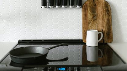 A lifestyle image of an induction hob with a saucepan, mug and chopping board resting on the surface