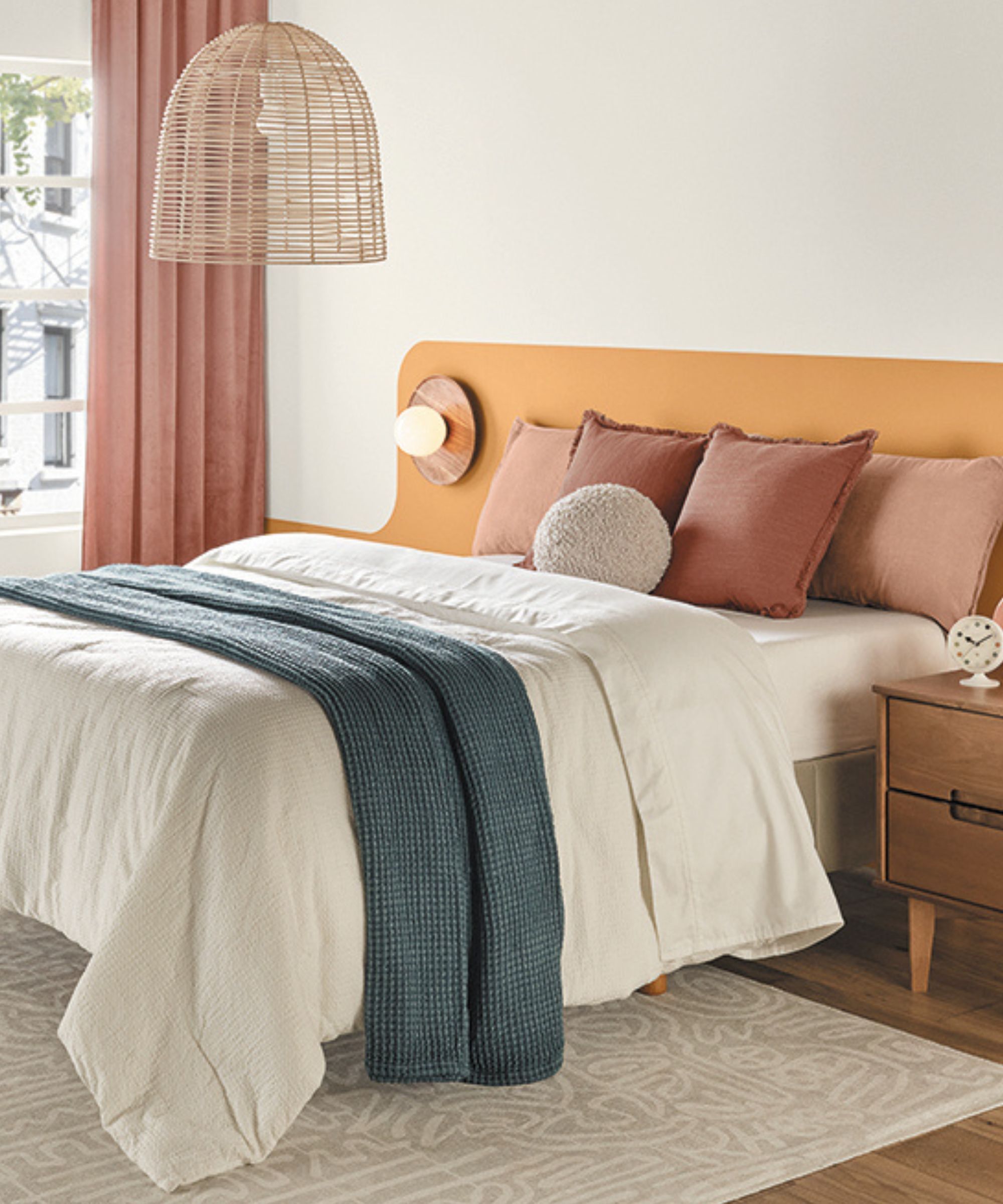 A modern bedroom with pale gray walls, a bed with an orange headboard and white bedding with a navy blue throw