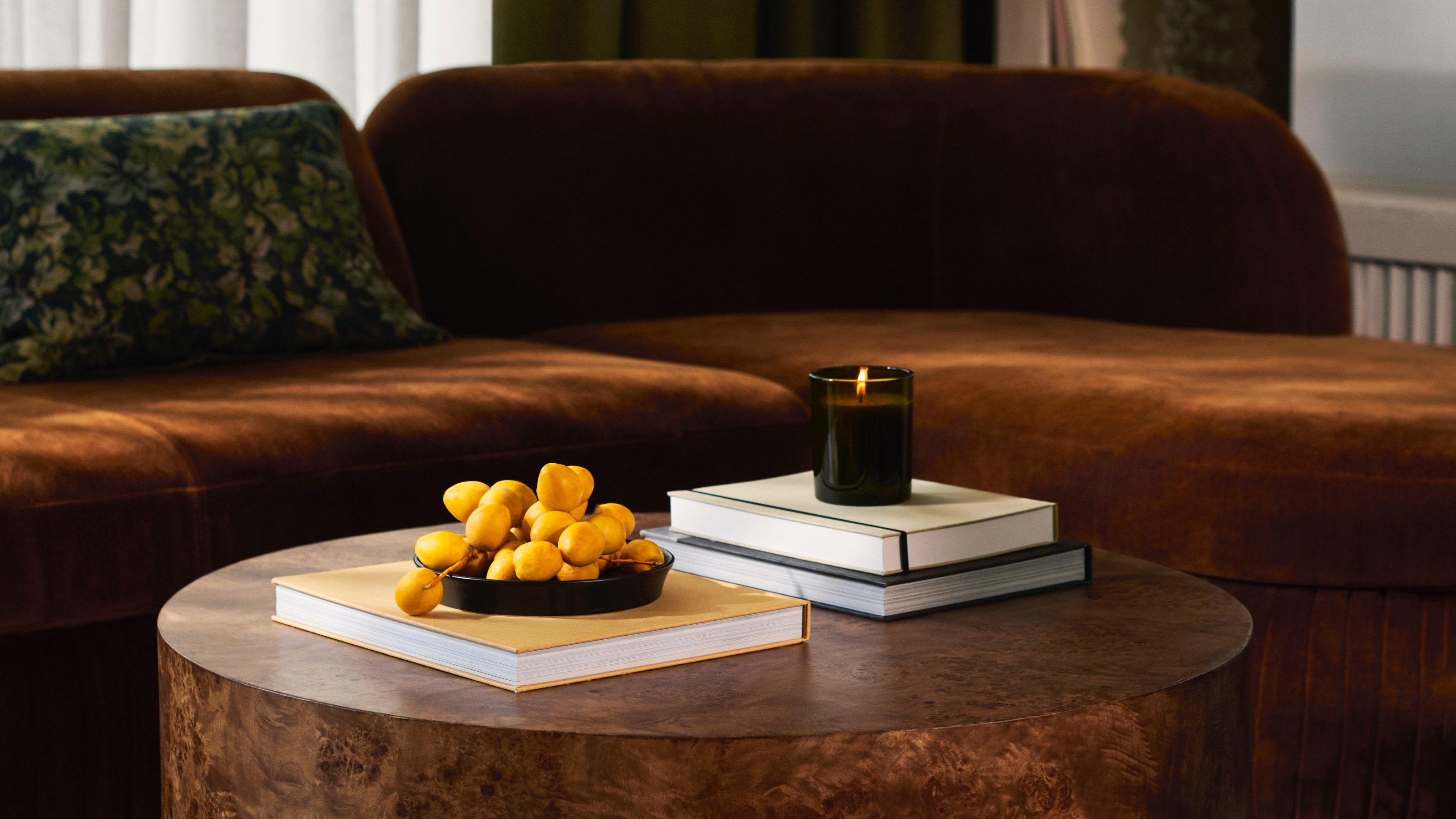 a coffee table with candle and books on in front of a rust-colored velvet sofa