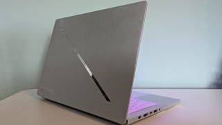 Back three-quarter view of Asus ROG Zephyrus G14 (2025) open on desk with green wall in background