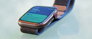 En Apple Watch SE med ett brunt armband ligger på en blank yta.