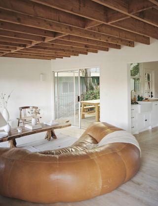 a modern neutral living space with a large leather sofa and an exposed wooden rafter ceiling