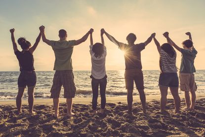 Friends holding hands above their heads and staring out into the ocean.