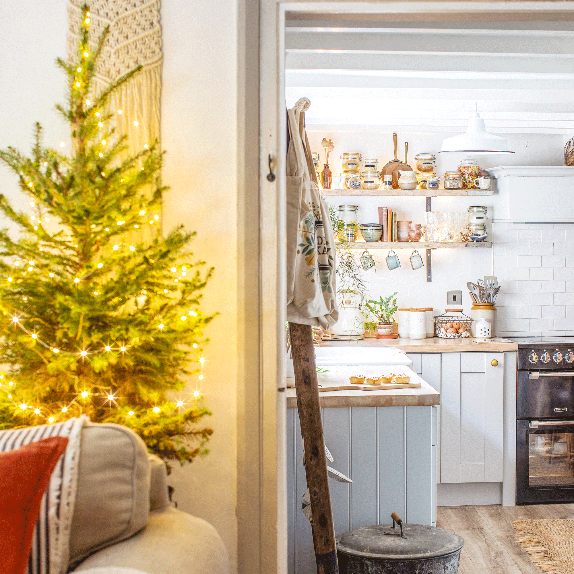 a living room with a small Christmas tree behind a sofa and a doorway leading into a kitchen