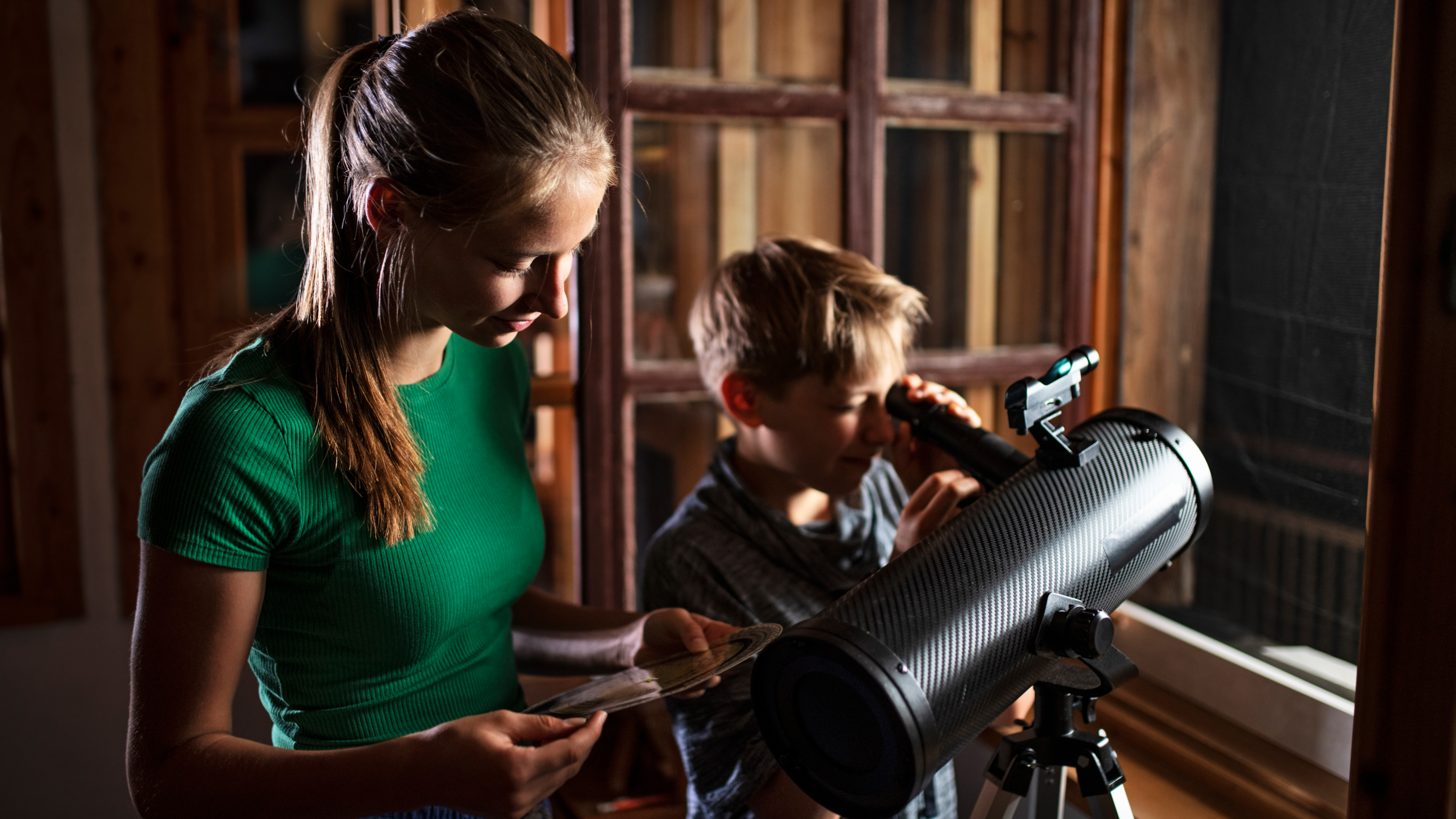 girl and boy using a telescope to look out a window