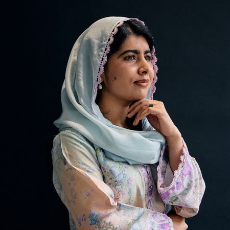 Malala Yousafzai poses in a blue headscarf and floral outfit against a dark backdrop