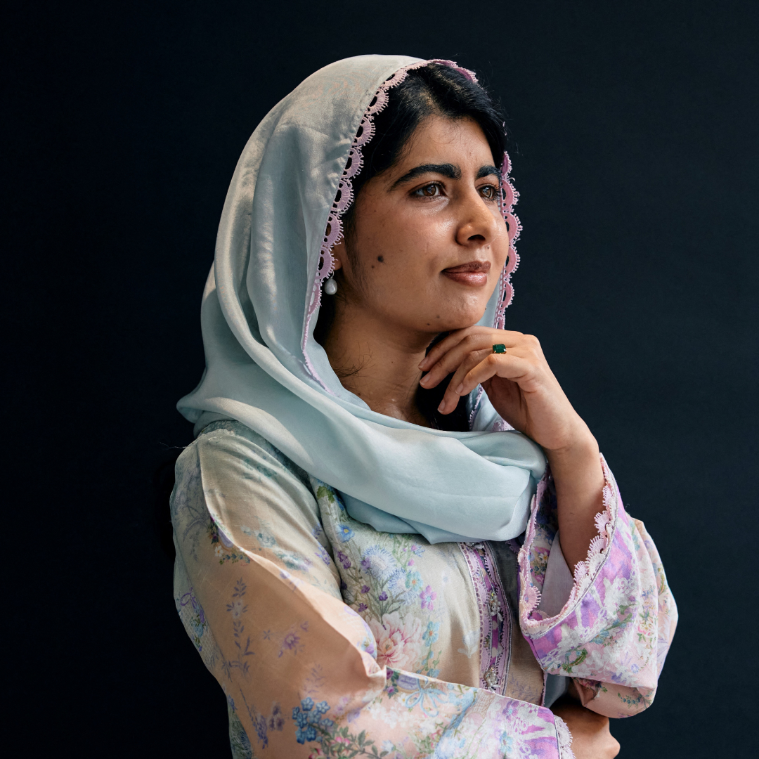 Malala Yousafzai poses in a blue headscarf and floral outfit against a dark backdrop