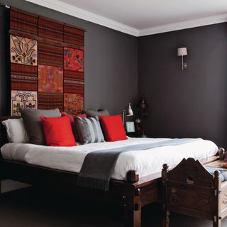 Grey bedroom, red fabric wall hanging, assorted cushions in red and grey