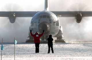 A giant LC-130 aircraft, equipped with enormous skis, prepares to take off from the ice.