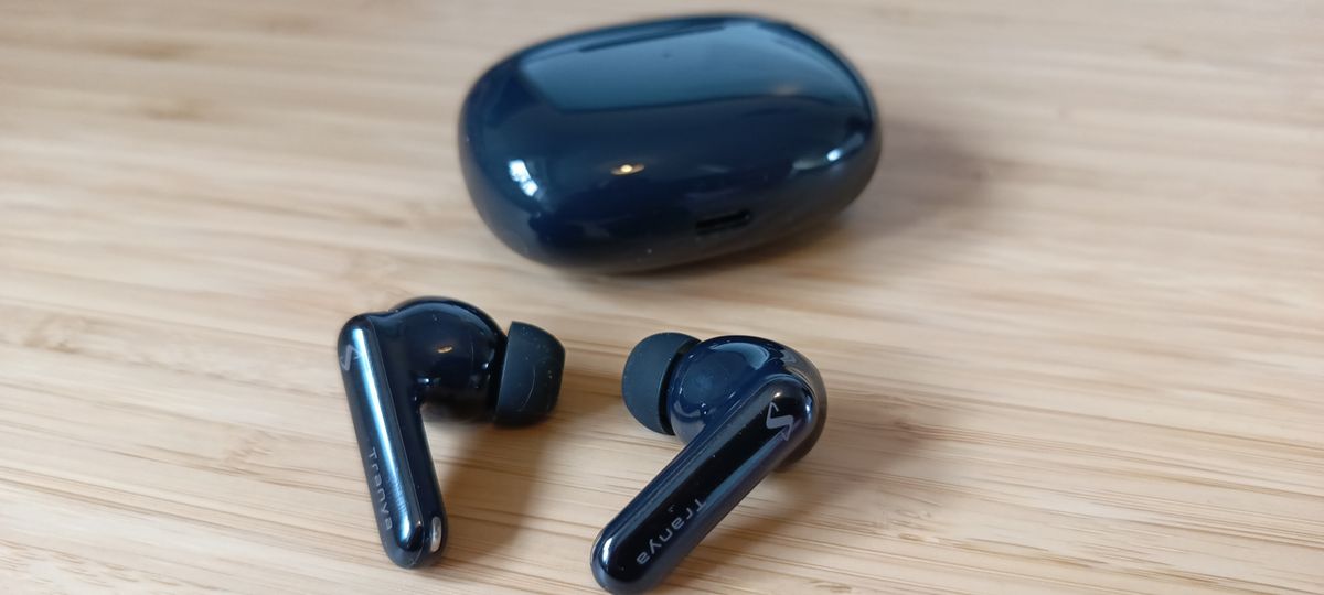 A pair of black Tranya Nova earbuds sitting on a wooden desk