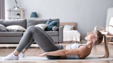 Woman doing Pilates hundred exercise on a yoga mat in a stylish, modern living room