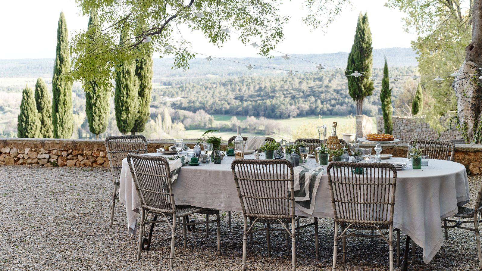 A large tablescaped table with white tablecloth on a gravel area overlooking a green landscape of trees and hills.