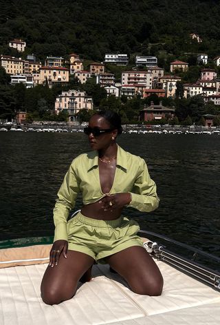 a photo of a woman's spring vacation outfit with green cropped linen shirt with matching shorts and black sunglasses and gold jewelry