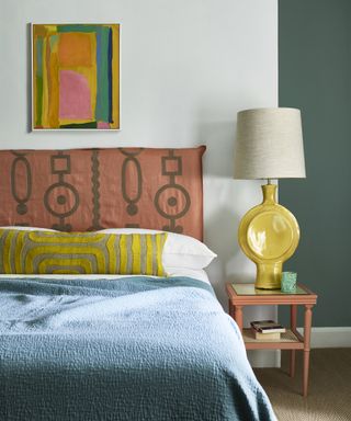 colourful bedroom with pink embroidered headboard and yellow bedside light, blue bedspread and colourful artwork