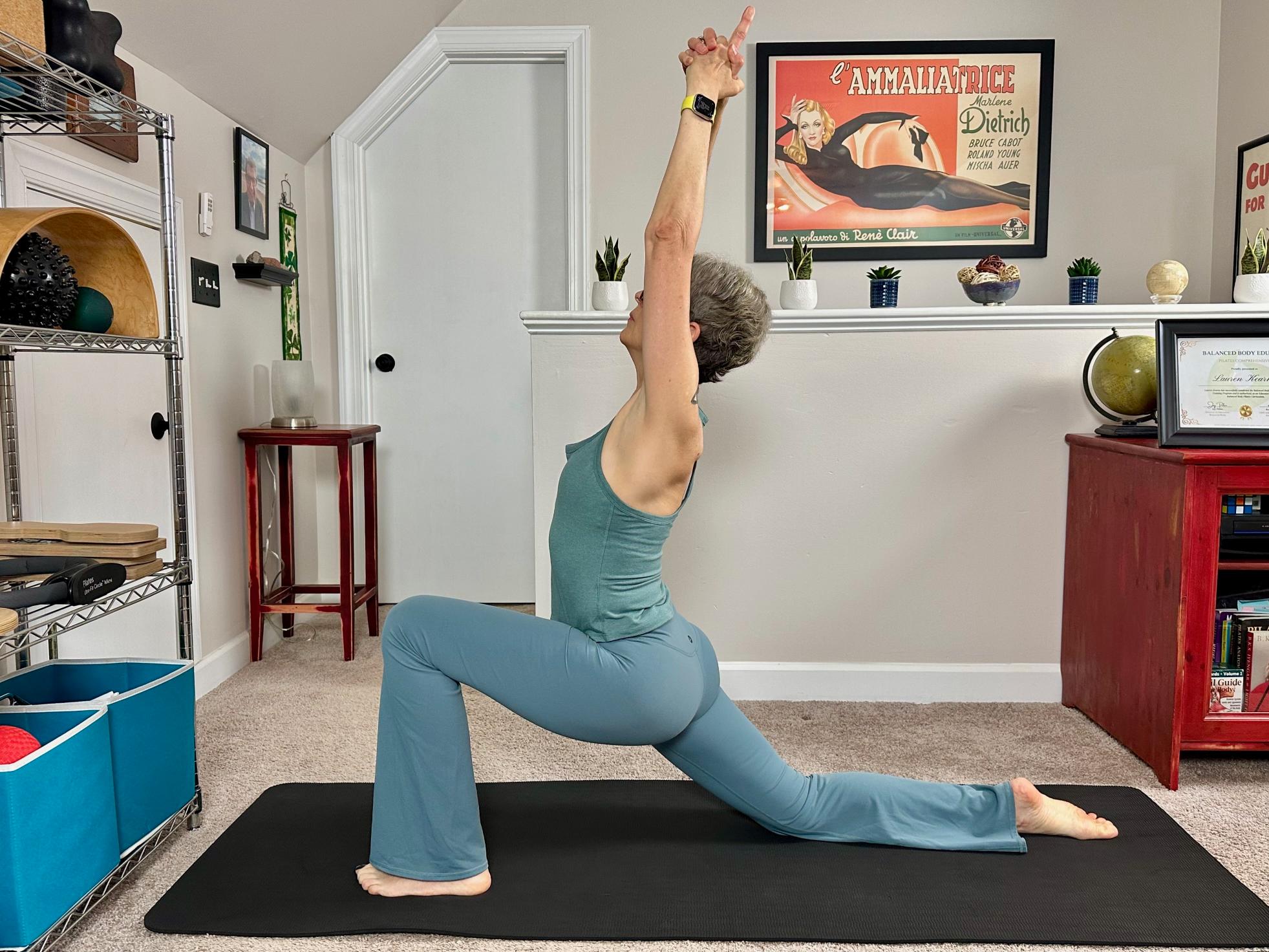 woman performing a low lunge with twist in a living room on a black yoga mat