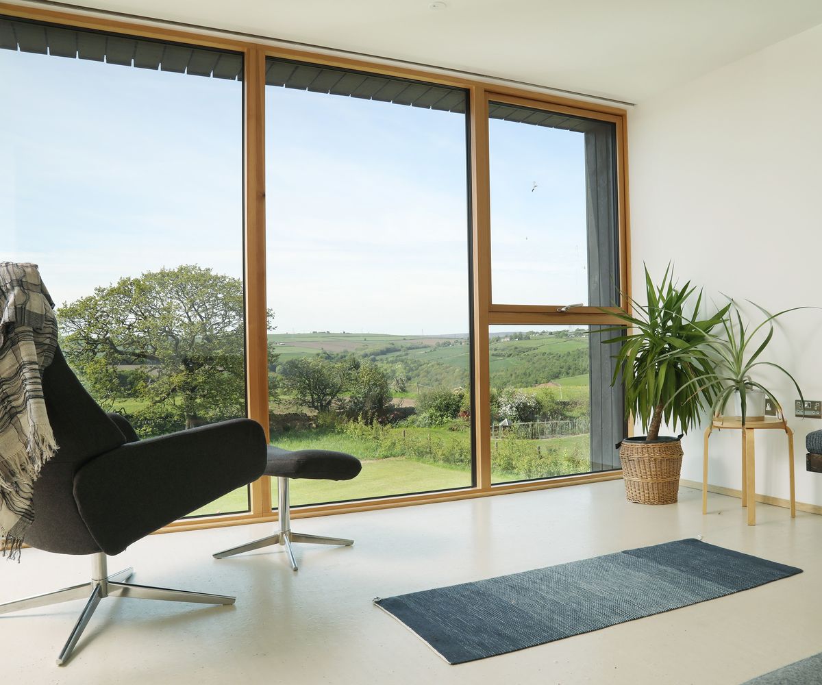 A dark swivel armchair sits in front of a wall of glazing looking out to the surrounding countryside
