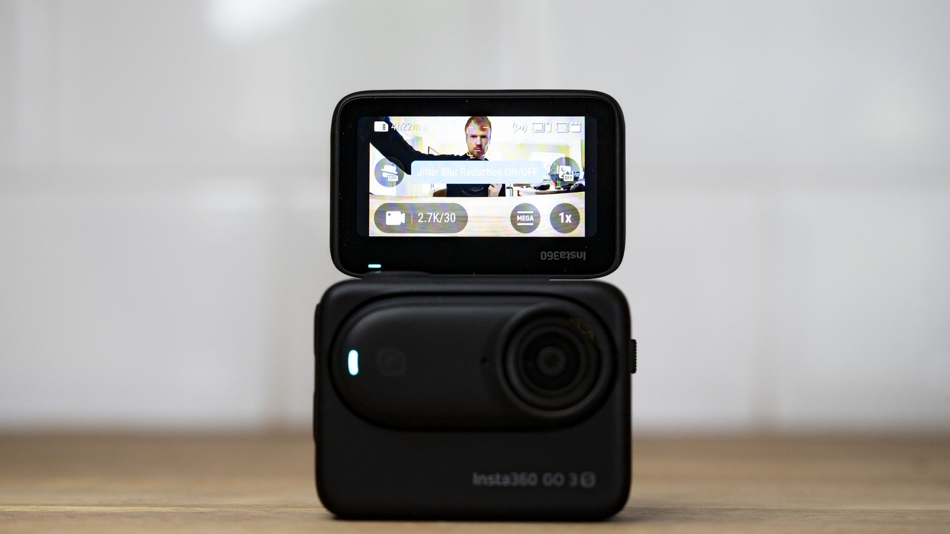 Insta360 Go 3S camera in its housing with rear selfie screen flipped upon a wooden surface