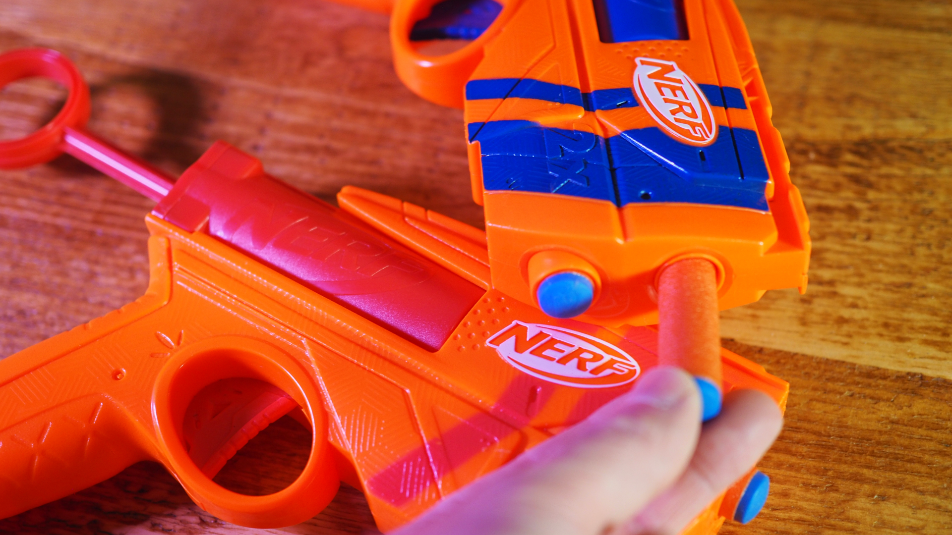 A hand loads one of the Nerf N-Series Duo Pack blasters on a wooden table