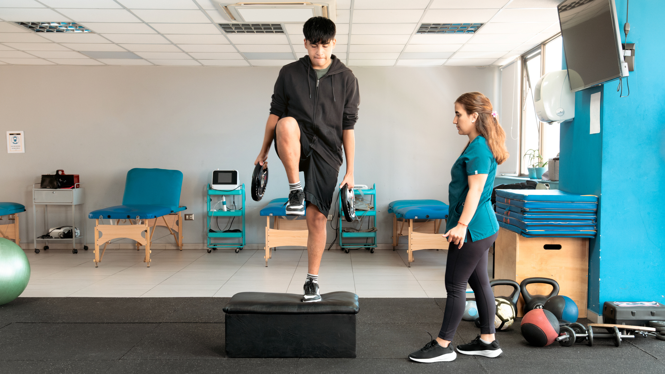 Medical professional observes a man performing the step-up exercise, holding weight plates by his sides