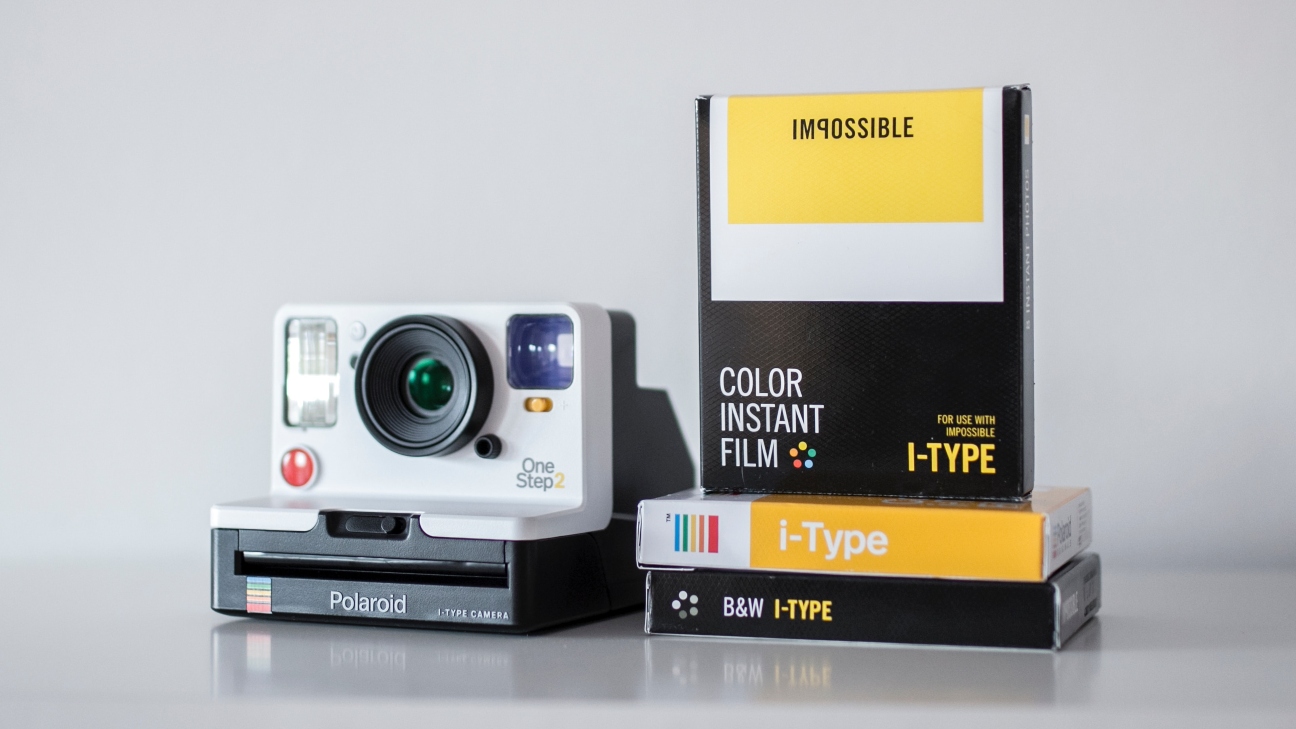 White polaroid camera on bench with three types of film next to it