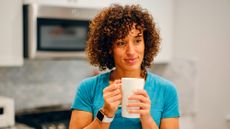 Woman in blue T-shirt stands in kitchen holding tall mug