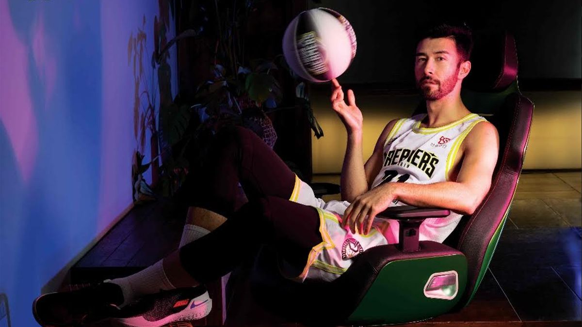 A man sits on a green chair twirling a basketball.