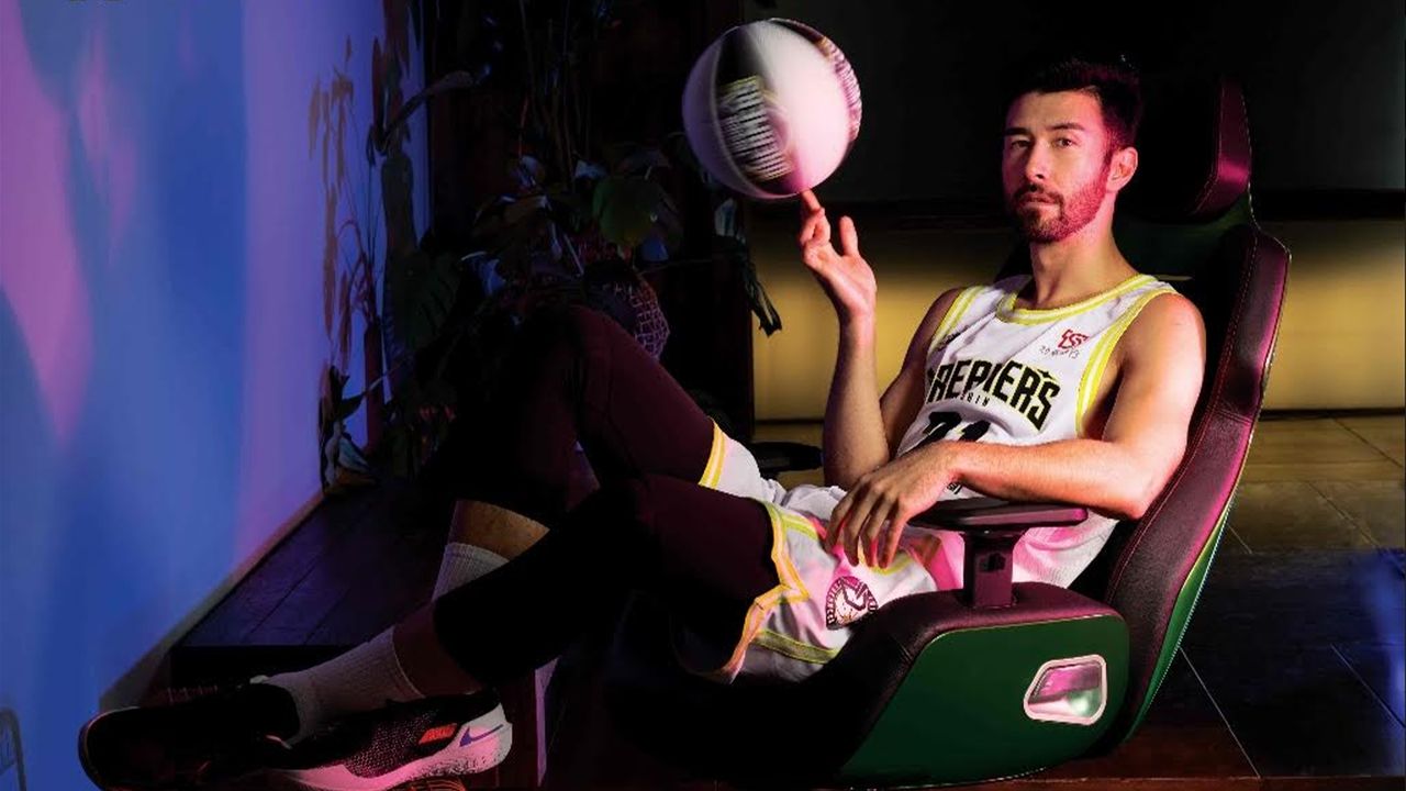 A man sits on a green chair twirling a basketball.