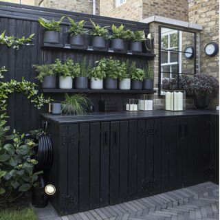 garden with grey tiles, black wooden fence with black shelving and black cabinets
