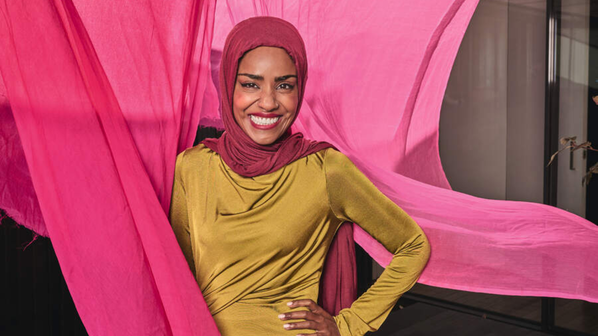 Nadiya Hussain standing in front of bright pink fabrics on a washing line 