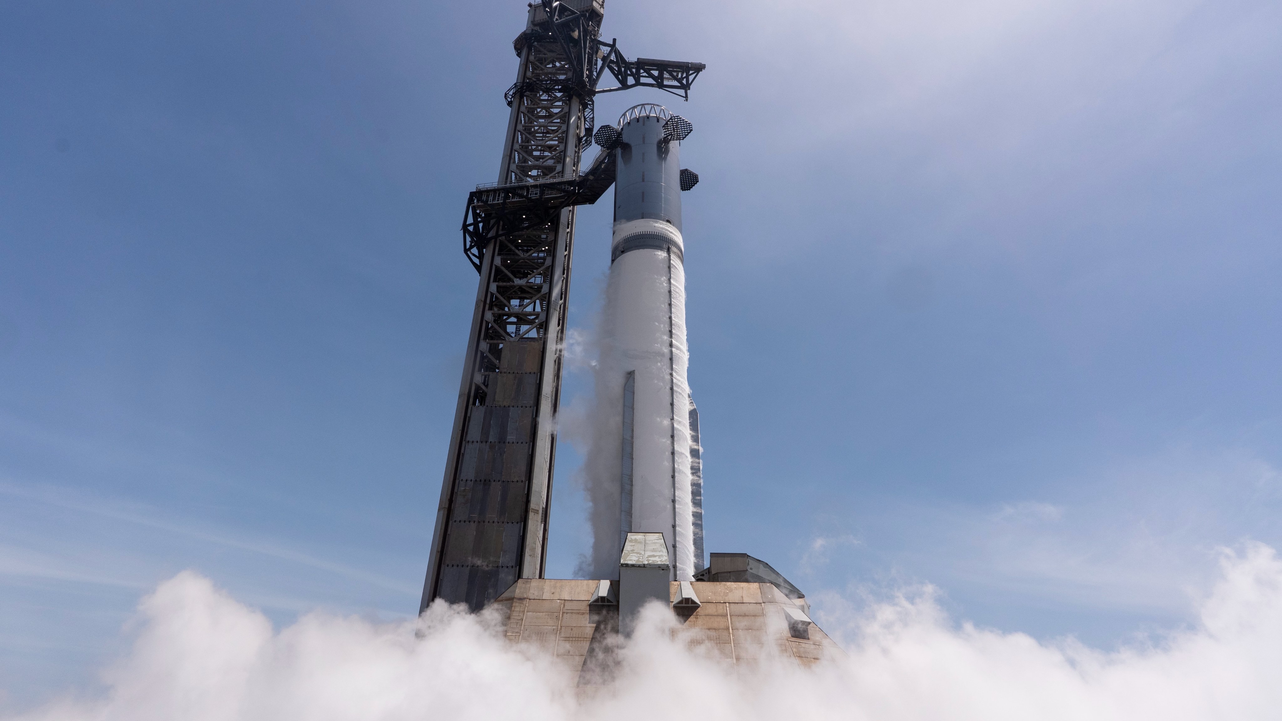 a large silver rocket fires its engines on the launch pad during a test