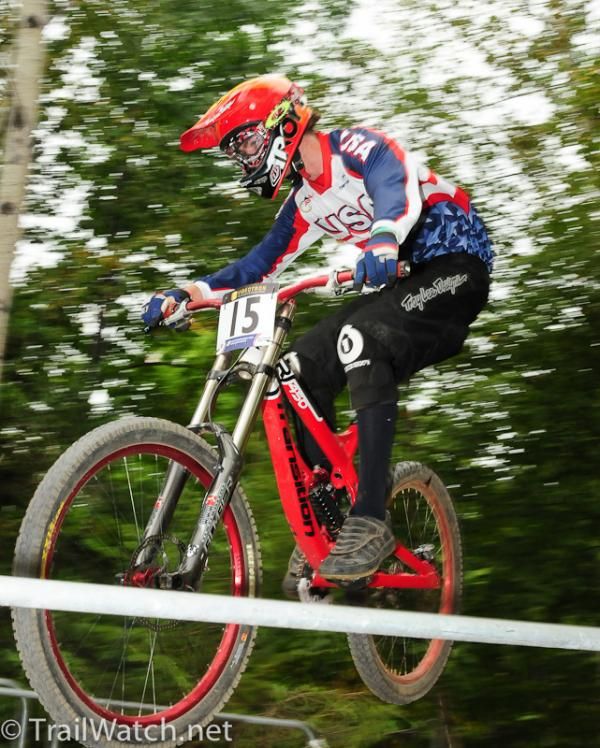 Downhill racers who are doing practice runs ride a jump that crosses the cross country course