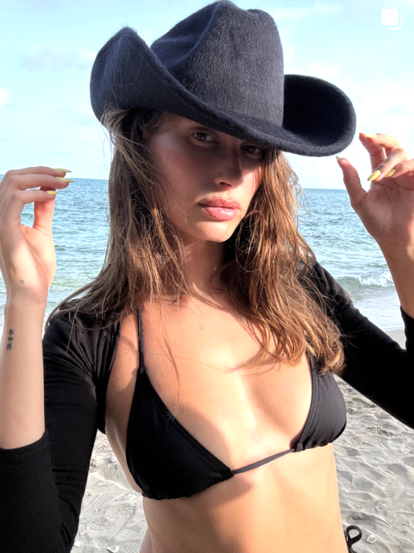 Hailey Bieber in a black bikini with a black cowboy hat and yellow nails